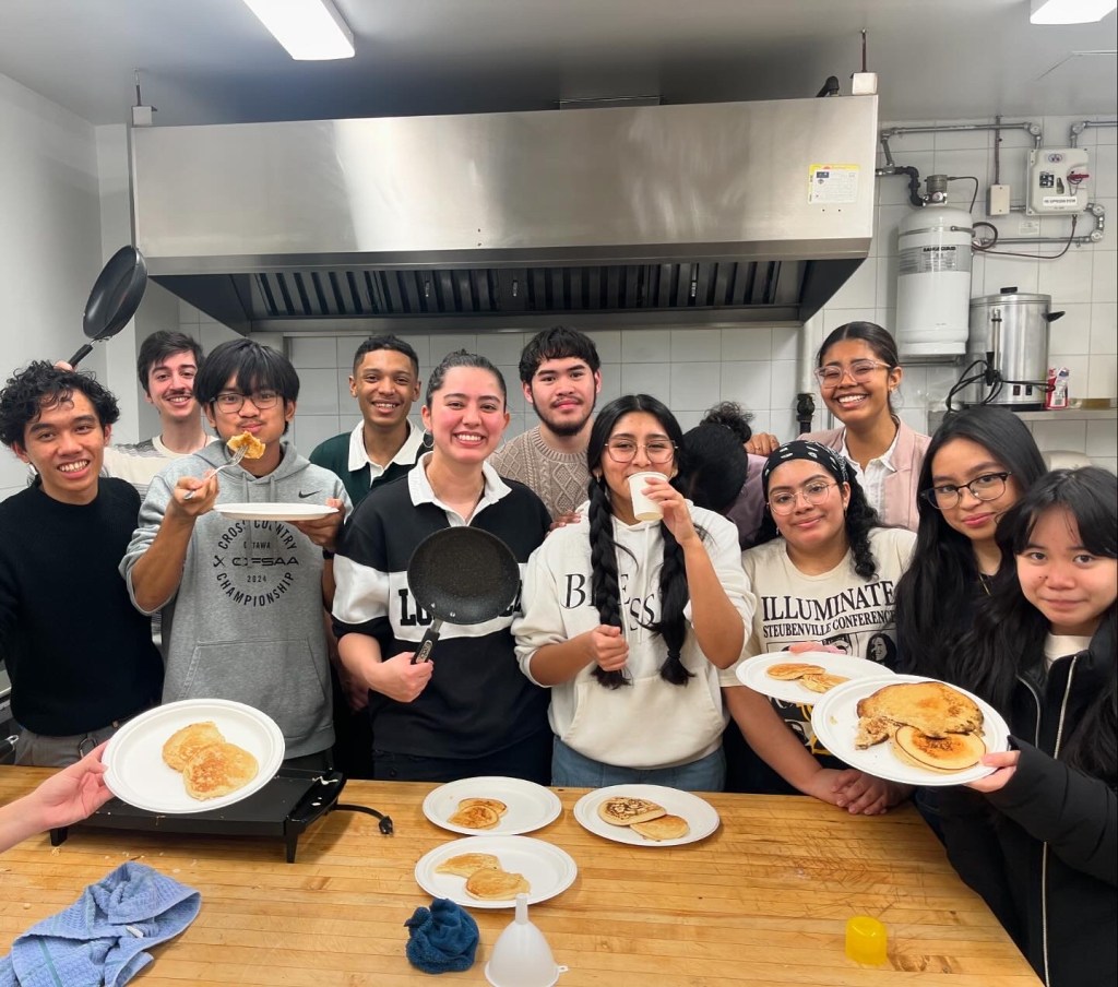 Young adults cooking and serving pancakes together in the parish kitchen